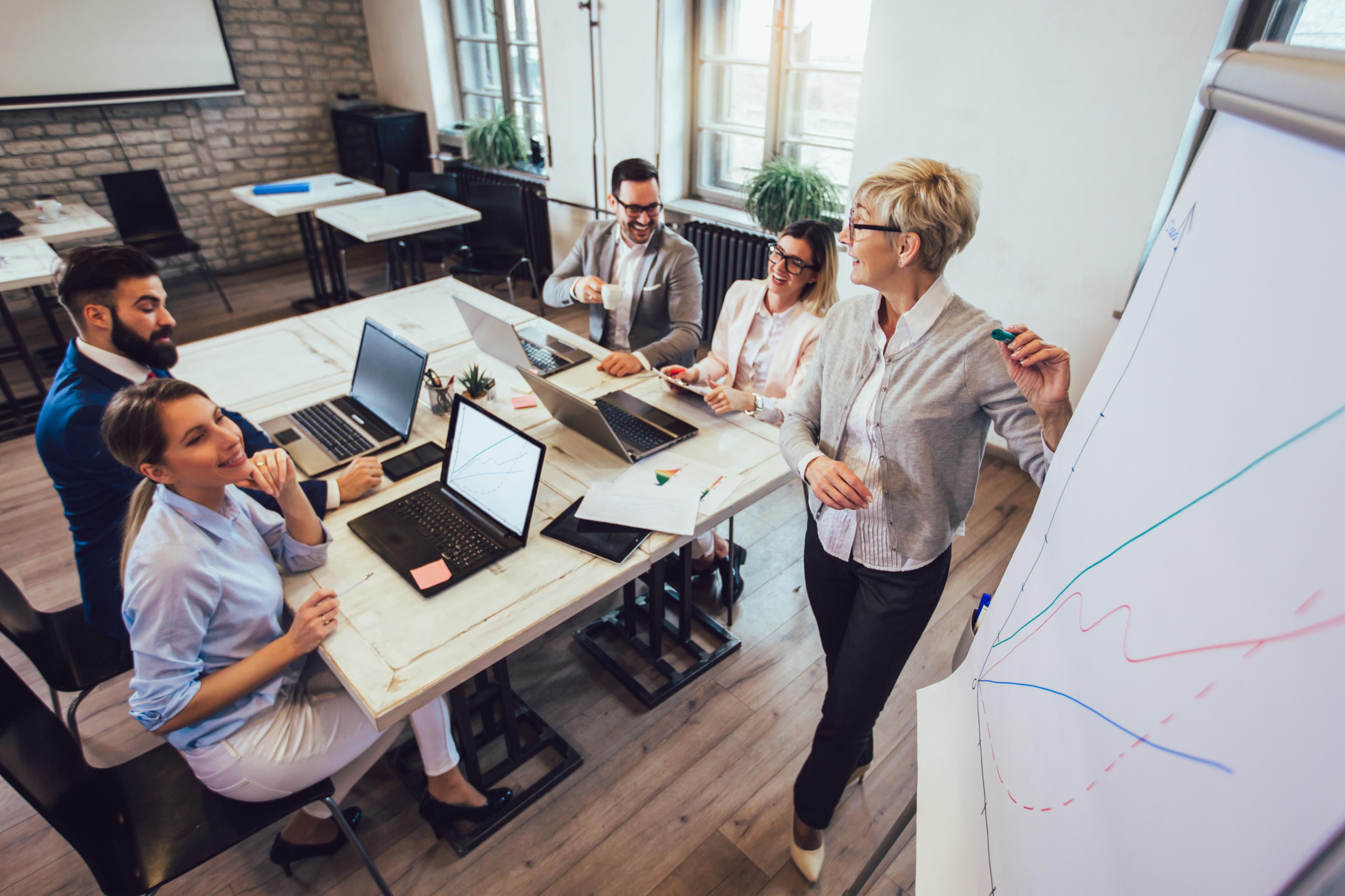 business team smiling at table together with laptops, being presented a line chart by a woman