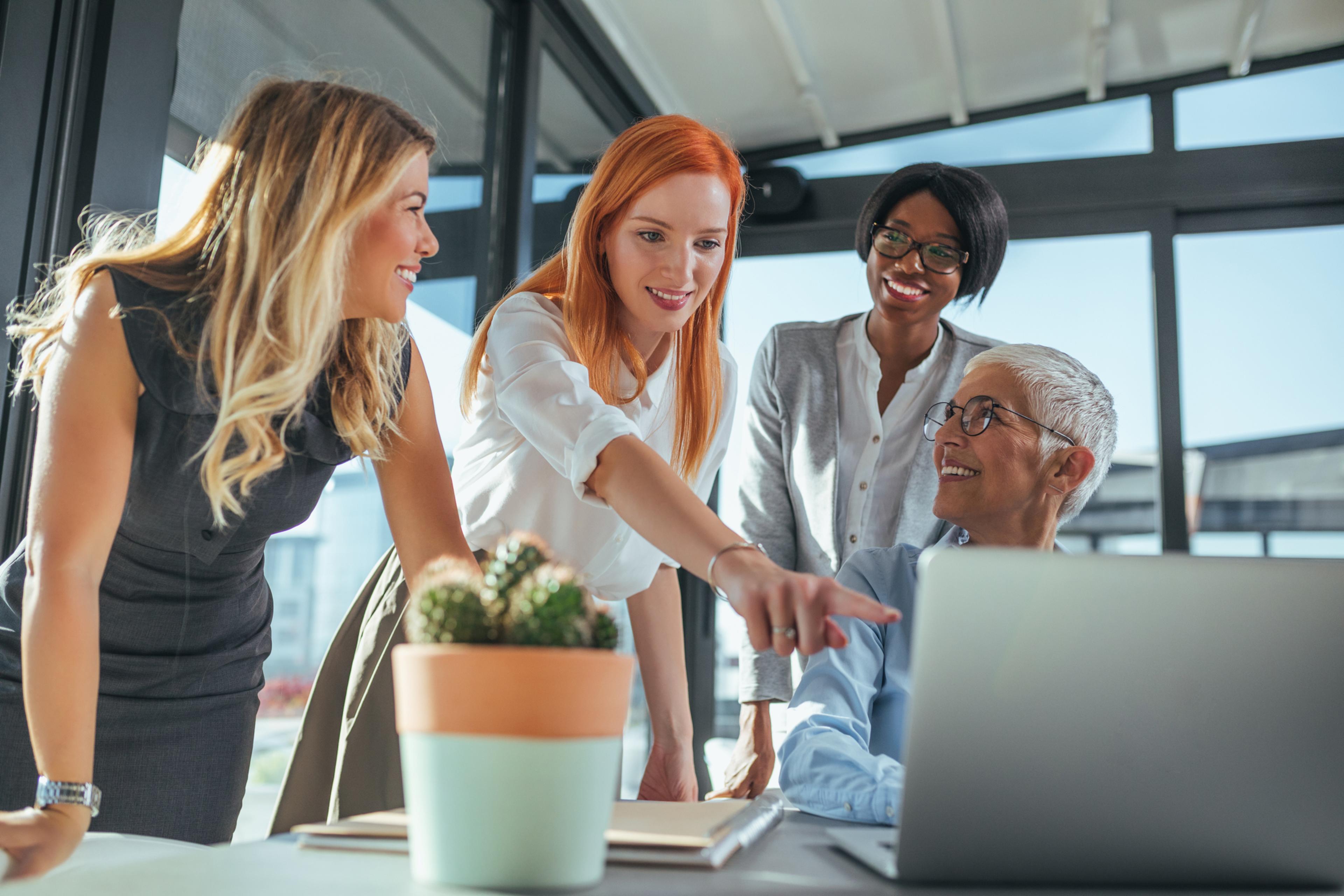 Four women around a laptop, with one pointing at the screen